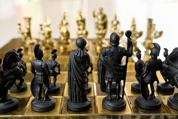 Back of black queen king centurion and knight chess piece figurines on chessboard facing gold opposing army