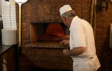 Pizza maker stands with his back to the camera and puts a pizza in the oven. Motion blur. Interior...