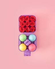 Creative concept of box of colorful Easter eggs on the one side and full of red roses on the other. Pastel color flat lay on spring pink background..