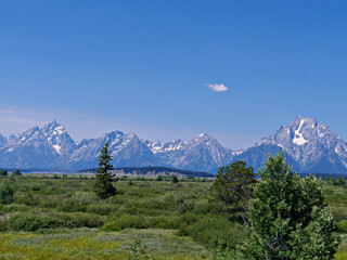 Fototapeta premium Snow-capped Grand Teton mountains in the distance seen from the road in Wyoming.