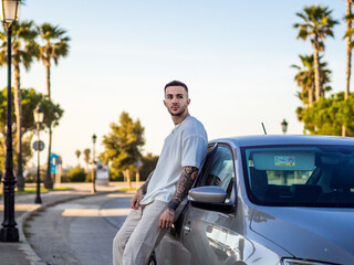 Spanish young man with tattoos leaning on the car