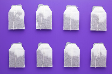 Tea bags with dry black tea on purple background. Top view, flat lay.