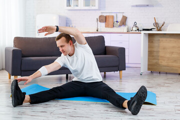 Muscular athletic man in a t-shirt doing warm-up exercises at home. Doing sports at home during the quarantine period. Fitness outside the gym