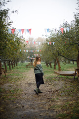 portrait of young beautiful caucasian woman with wavy hair in the garden. a girl in a warm sweater stands with an open shoulder in the middle of a park or on her ranch. autumn fair in the garden
