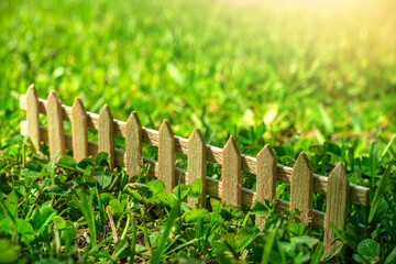 miniature wooden fence on the green grass, summer weather, the sun is shining.
