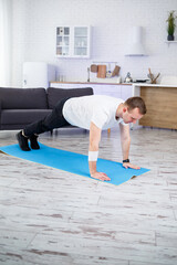 Handsome muscular man in a t-shirt doing functional plank exercises on the floor at home. Fitness at home. Healthy lifestyle.