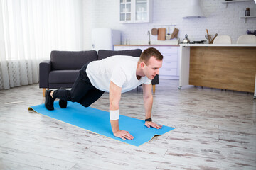 Fototapeta na wymiar Handsome muscular man in a t-shirt doing functional plank exercises on the floor at home. Fitness at home. Healthy lifestyle.