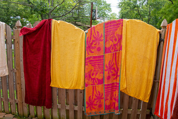 Colorful towels spread opened and hanging on a wooden fence near a backyard swimming pool on a sunny summer day