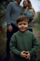 Asian cute boy playfully looks to the side. a child in a warm jacket holds hands and smiles. boy on the background of parents
