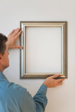 Man hanging silver frame on wall