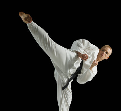 Young man performing karate kick on black background