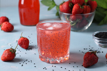Beverage with strawberries and basil seeds in a glass and bottle on light blue background. Closeup