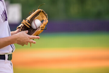 A young adult male baseball player holding a baseball glove and baseball ball in his glove.