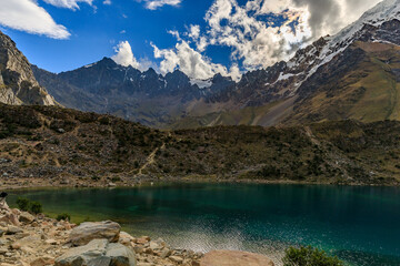 Sunny sky with beautiful white clouds looking over the snowy Salkantay mountain range and peak and the cold blue waters of the Humantay Lake in Peru