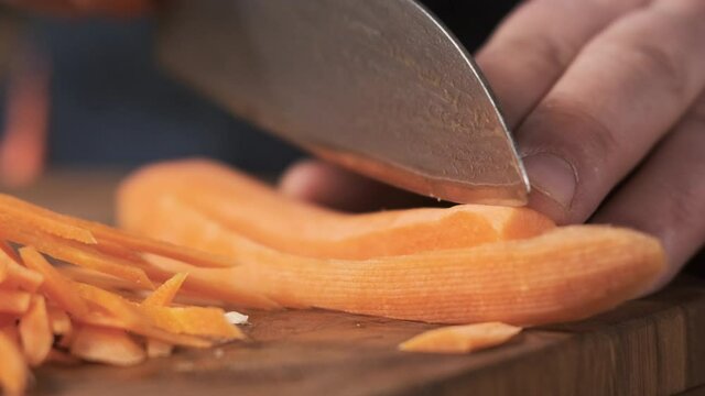 Extreme close up macro chef in restaurant kitchen cuts carrot with sharp, shiny knife. man prepares food for family and cuts celery on wooden cutting board, vegetarian food salad.