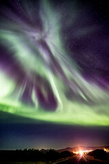Magical Aurora Borealis or Northern Lights, long exposure in the summer night in Western Iceland, distant town lights in the background