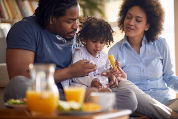 A cute little girl sitting in the lap of their parents at home and enjoying making soap bubbles. Family, home, playtime