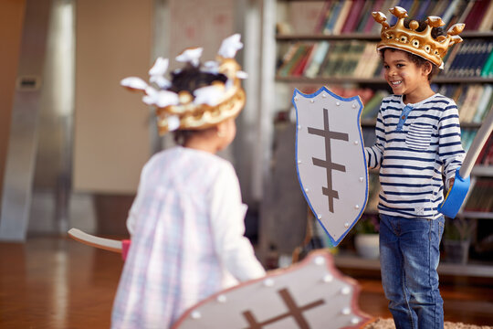 A little brother and sister dressed like knights are having swords fight game while playing at home. Family, home, playtime
