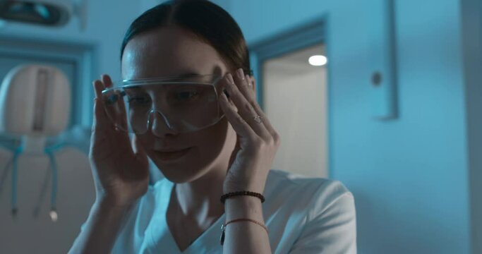 A female medical worker is standing in a dark room she is takes a disposable glasses to wear it.