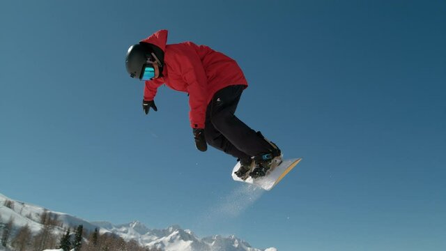 SLOW MOTION CLOSE UP: Extreme snowboarder jumping in big mountain ski resort. Detail of snowboard taking off the kicker in groomed snow park. Snowboarding jump on sunny winter day in snb park