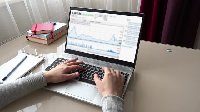 Market indexes. Financial schedules and charts. The girl working at home office hands on keyboard. Out of focus.