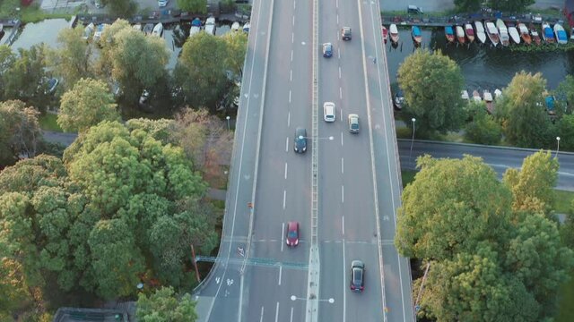 Cars driving over a bridge in Stockholm, Sweden. Summer late in the day sun with an aerial drone view of the highway, park, lake and city.