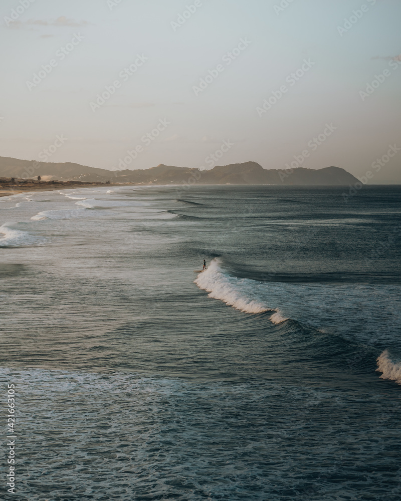 Poster Aerial shot of a surfer on the wavy sea or lake on the background of mountains