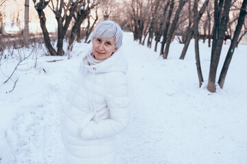 Happy middle-aged woman walks in the winter in the city snow-covered park. Winter walks during the holidays