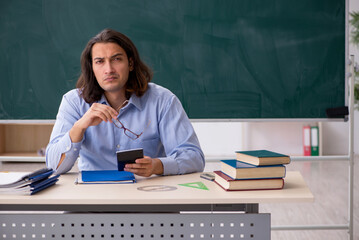 Young male teacher in front of green board