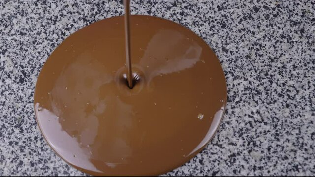 confectioner pours melted milk chocolate on granite table for tempering. Chocolatier stirring with spatula tempered liquid chocolate top view. Cook tempers chocolate
