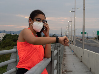 latina girl checks her watch while talking on the phone on a bridge after a run
