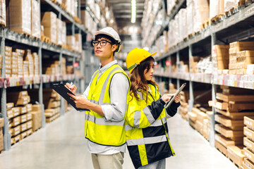 Asian two engineer in helmets team order details on tablet computer for checking goods and supplies on shelves with goods background in warehouse.logistic and business export