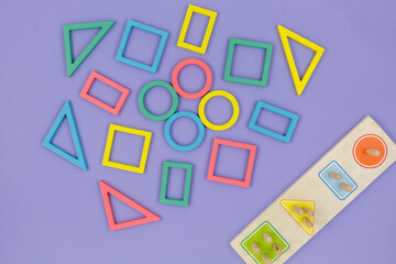 Multicolored wooden toys, blocks on violet background. Trendy puzzle toys. Geometric shapes: square, circle, triangle, rectangle. Educational toys for kindergarten, preschool or daycare. Close up