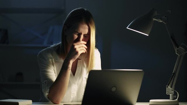 Late work. Night insomnia. Project deadline. Workaholic lifestyle. Tired exhausted sleepy female employee yawning using laptop typing at dark workplace with desk lamp light in home office.