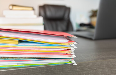 Colorful folders of finance data documents stack on manager table with blurred office background....