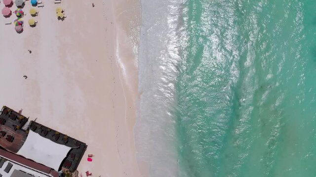 Aerial top view of paradise beach with umbrellas and turquoise ocean, Nungwi, Zanzibar. Tropical landscape with people, parasols, sand, and blue water. Coastline of luxury hotels near clear blue water