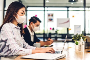 Young asian business woman using laptop computer working and planning meeting in quarantine for coronavirus wearing protective mask with social distancing while sitting on office desk