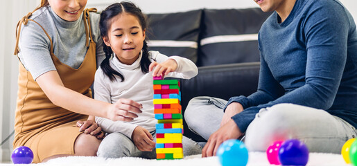 Portrait of enjoy happy love asian family father and mother with little asian girl smiling playing with toy build wooden block board game in moments good time at home