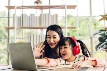 Mother and asian kid little girl learning and looking at laptop computer making homework studying knowledge with online education e-learning system.children video conference with teacher tutor at home