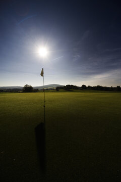 Beautiful scenery of a golf hole and a flag in a field against a bright sunny day background