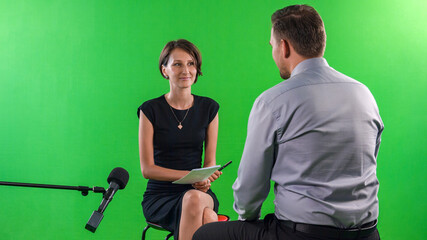 Young female presenter interviewing in television studio with green screen