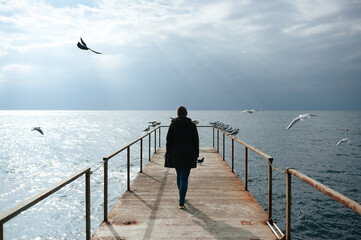 The girl walks along the pier to the sea, the seagulls fly away