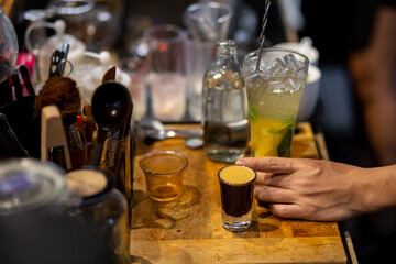 A close-up of a lemon-soda cold drink in a clear glass on the cafe table where the barista is mixing something into the glass. Summer refreshing drink