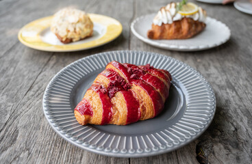 Close-up of Raspberry Croissant and others on wooden table. Croissant is a French buttery, flaky and crescent-shaped bread.