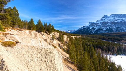 Eroded Sandstone Cliffs and Green Forest with Rundle Mountain Range on Skyline.  Sunny Springtime Panoramic Landscape in Canadian Rockies, Banff National Park