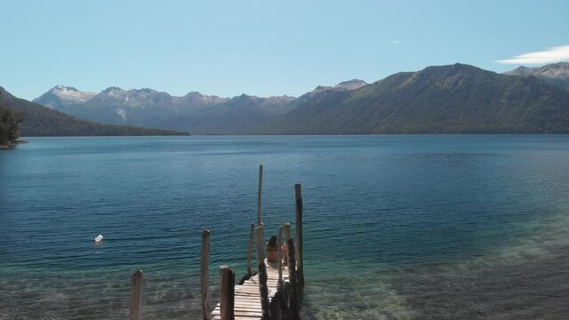 Couple of women sitting on a wooden dock contemplating the landscape of a turquoise lake in patagonia.