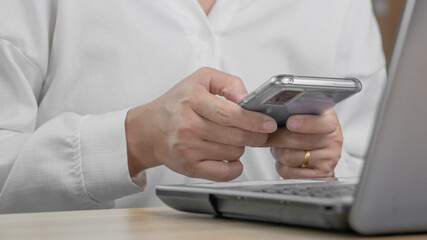 Close up of female business typing on the phone while working on a laptop computer in her office.