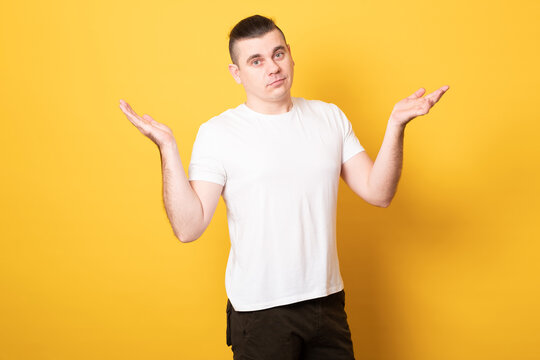 Young handsome man wearing white t-shirt standing over isolated yellow background clueless and confused expression with arms and hands raised. Doubt concept.