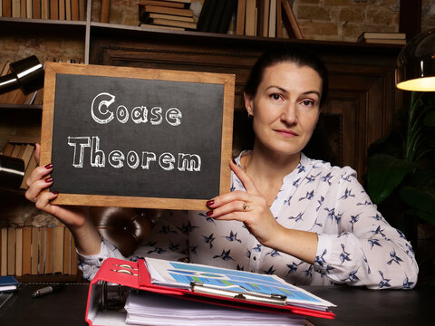 Hand holding chalkboard with phrase Coase Theorem .