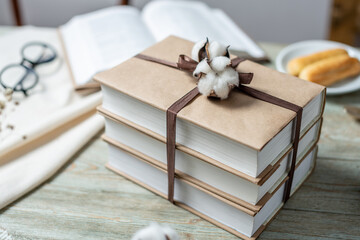 A stack of beautifully wrapped craft paper books, tied with ribbon and decorated with cotton, on a...